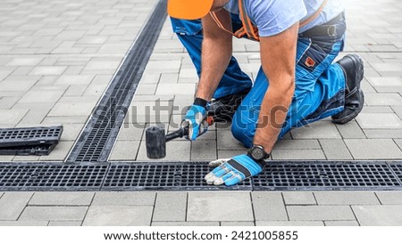 Laying interlocking paving. A worker is placing the grutter grid to drainage channel.