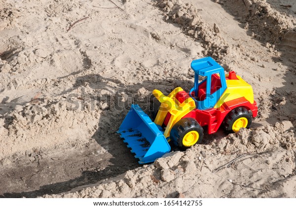 Laying the road. Tractor on construction of new\
road. Children\'s bright plastic excavator in the sandbox. Playing\
yard construction in the\
sand.