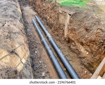 Laying Of Underground Communications For Residential Buildings. Plumbing Pipes Of Black Color Are Buried Deep In An Earthen Ditch.