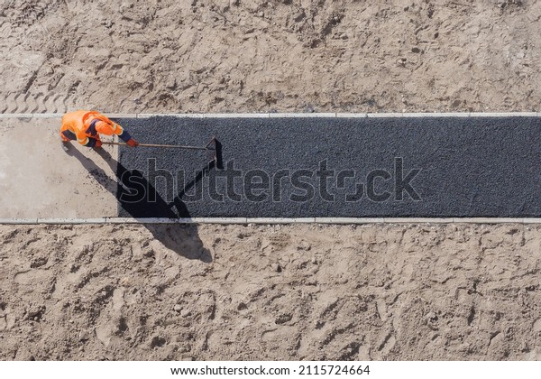 Laying worker new asphalt paving road construction\
site work pathway. New road construction worker laying asphalt\
surface on walkway work path. Sidewalk construction asphalt work\
tarmac road worker