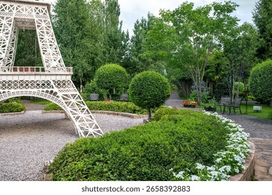The layout of the Eiffel Tower is surrounded by trees and flowers against the background of the cloud sky.