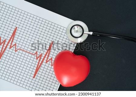 Layout of an electrocardiogram, stethoscope and a heart-shaped model on black background