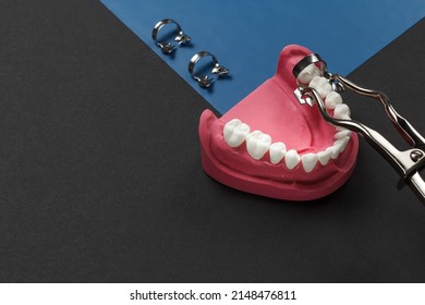Layout of the human jaw and a rubber dam clamp pliers, a rubber dam with dental dam clamps on the black background. Medical tools concept. Top view.