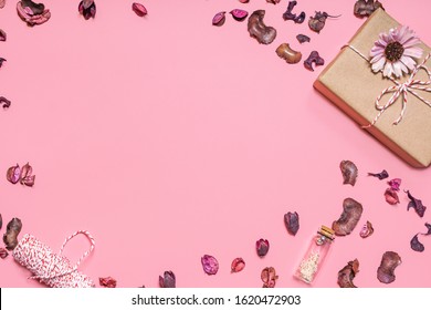 A layout of a present with strings, bottle, flowers and dry flower petals laying on a pink background, representing copy space of gifts for Christmas, valentine’s day, birthday and special events 