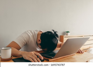 Lazy Asian Man Is Working With Laptop In His Apartment Bedroom In Concept Of Work From Home And Work At Home.