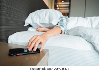 Lazy Asian Young Woman Trying To Snooze Awaking Alarm Clock In Smartphone Close Up, Woman Wake Up Late In Morning Up To 8.00 Am. Tried Woman Sleeping On The Bed In Bedroom.