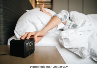 Lazy Asian Young Woman Trying To Snooze Awaking Digital Alarm Clock On The Table Beside The Bed Close Up, Woman Wake Up Late In Morning Up To 8.00 Am. Tried Woman Sleeping On The Bed In Bedroom.