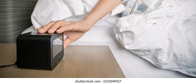 Lazy Asian Young Woman Trying To Snooze Awaking Digital Alarm Clock On The Table Beside The Bed Close Up, Woman Wake Up Late In Morning Up To 8.00 Am. Tried Woman Sleeping On The Bed In Bedroom.