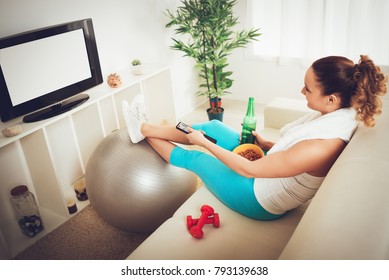 Lazy Beautiful Young Woman In Sport Clothing Sitting Front Of The TV And Doesn't Wont To Exercise.