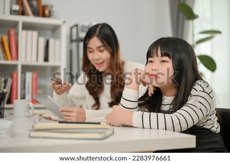 Lazy and bored young Asian girl sits at a table with her hand on her chin, too tired to study or do her homework. education and childhood concept
