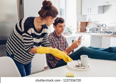 Lazy Boyfriend Hanging In Phone While His Girlfriend Cleaning His Dishes After Dinner In Kitchen. Inequality Of Men's And Women's Rights. Family Arguement