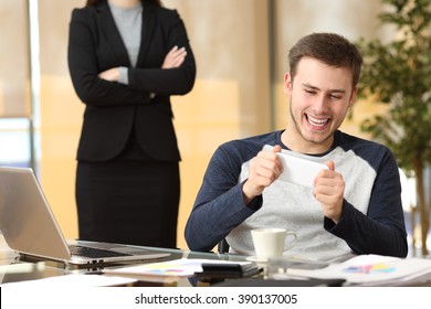 Lazy employee playing games with his smartphone sitting in a desktop while his angry boss is watching at office - Powered by Shutterstock