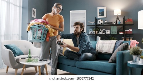 Lazy Husband Playing Videogames And Relaxing On Sofa While His Wife Is Doing Household Chores, Gender Inequality Concept