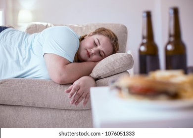 Lazy lifestyle. Stout red-head woman sleeping on the couch after eating all junk food