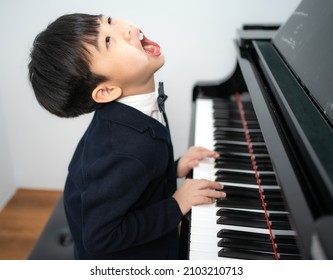 Lazy Little Boy In Black Suit Sitting At Grand Piano Makes Funny Face. Cute Boring Kid Pianist Feels Tired To Practice Playing Classic Keyboard. Playful Child Musician Refuses To Perform A Concert.