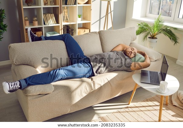 Lazy man enjoying a nap. Tired man
sleeping on the sofa at home. Young guy falls asleep on the couch
while working on his laptop computer in the living
room