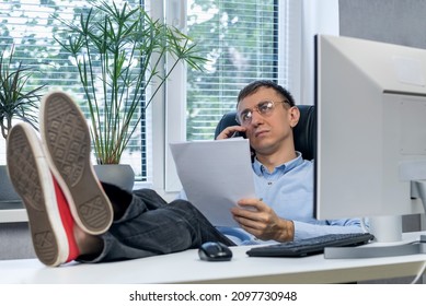 Lazy Man Feet Up On Desk Examines Papers And Talking On The Phone. Young Director Working With His Feet On The Table