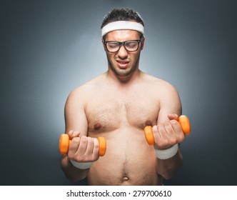 Lazy Man Try To Exercising And Doing Fitness. Obesty Man Using Small Dumbbells For Bodybuilding. Dark Gray Background. Studio Shot