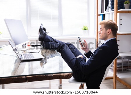 Lazy Man Using Phone At Work Desk Instead Of Working