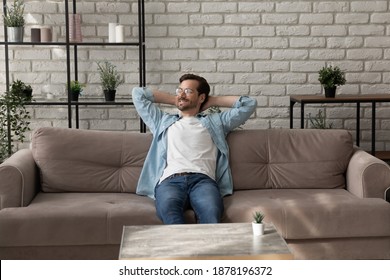 Lazy morning. Successful millennial man relaxing on comfy sofa at home after finishing work looking aside with glad smile. Calm young guy taking pleasure in awaited weekend enjoying peaceful dreams - Shutterstock ID 1878196372