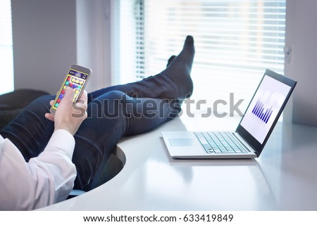 Lazy office worker playing mobile game with smartphone during work hours. Avoiding his job and being lazy with feet and socks on table. Useless and relaxing man doing nothing and forget his job.