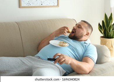 Lazy overweight man with donuts watching TV on sofa at home
