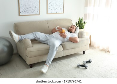 Lazy overweight man eating chips on sofa at home