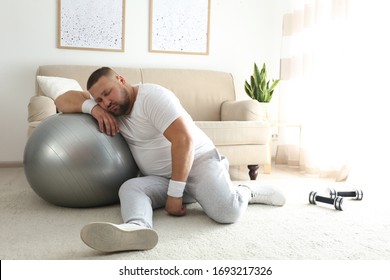 Lazy overweight man with sport equipment sleeping on floor at home