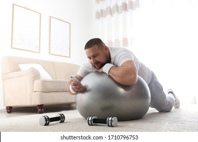 Lazy Overweight Man Using Smartphone While Lying On Exercise Ball At Home