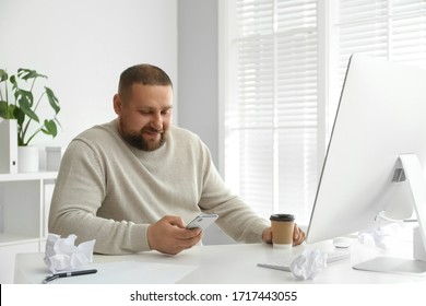 Lazy overweight office employee with smartphone at workplace
