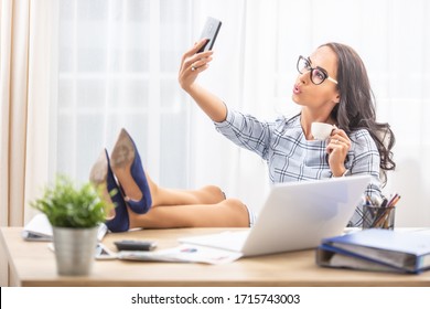 Lazy secretary with her feet up taking a selfie with a coffee in her hand.