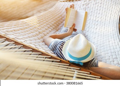 Lazy time. Man in hat in a hammock with book on a summer day - Powered by Shutterstock