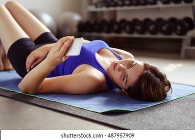 Lazy Or Tired Woman Laying On Back While Looking At Something On Her Phone At Gym