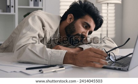 Lazy weary sleepy male manager tired exhausted Arabian Indian businessman employee working computer boring remote job man fall sleep on desktop napping in office overwork fatigue no energy sleeping