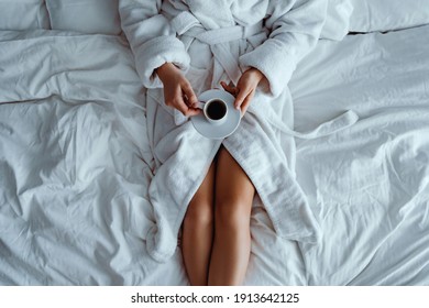 Lazy woman wearing bathrobe lying on bed and enjoying aromatic coffee cup during relaxing at cozy comfort bedroom at hotel room. Easy lifestyle. Beginning of new day