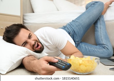 Lazy Young Man With Bowl Of Chips Watching TV While Lying On Floor At Home