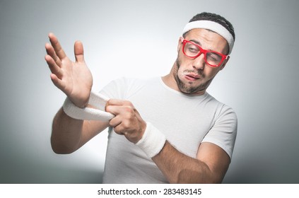 Lazy Young Man Does Not Wish To Doing Fitness - Exercising.
Funny Sport Guy Get Undressing
Isolated On Gray Background. Studio Shot.
Nerd Doing Aerobics