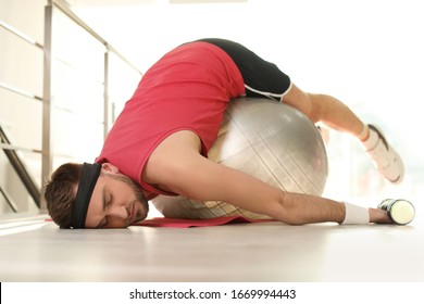 Lazy Young Man With Exercise Ball On Yoga Mat Indoors