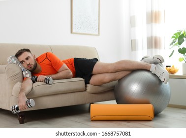 Lazy Young Man With Sport Equipment On Sofa At Home