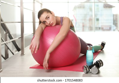 Lazy Young Woman With Exercise Ball On Yoga Mat Indoors