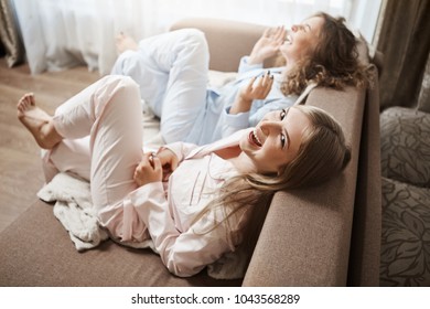Lazy-bones Doing Nothing And Enjoying Leisure Together. Upper-angle Shot Of Cute Women Sitting In Sofa In Nightwear Laughing Out Loud, Talking About Awkward Moments In Office, Spending Weekends
