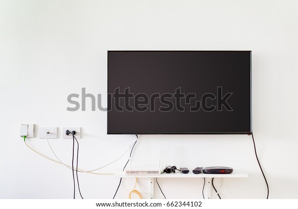lcd tv on wall with remote, wireless internet access\
point and set top box