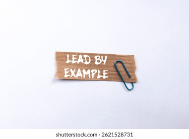 Lead by example message written on ripped torn brown paper piece on white background. Conceptual lead by example symbol. Copy space.