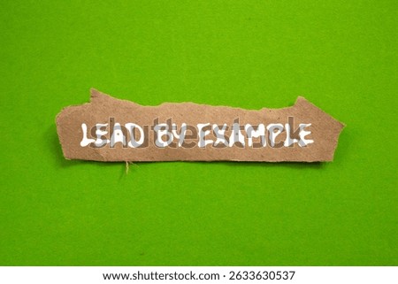 Lead by example message written on ripped torn brown paper piece on green background. Conceptual lead by example symbol. Copy space.
