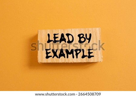Lead by example message written on wood piece on orange background. Conceptual lead by example symbol. Copy space.