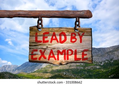 Lead by example motivational phrase sign on old wood with blurred background