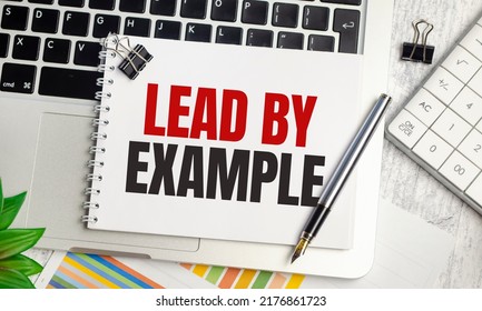 Lead By Example Text On Notepad And Laptop On Wooden Background