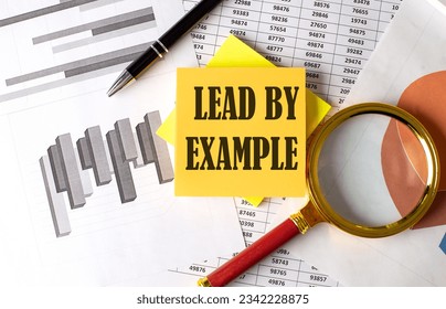 LEAD BY EXAMPLE text on sticky on the graph background with pen and magnifier
