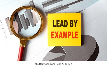LEAD BY EXAMPLE text on sticky on red notebook on chart background