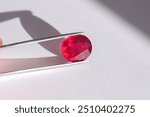 Lead glass filled natural ruby gemstone in tweezers. Heated, treated, affordable red gemstone. Mass market ruby gemstone mined in Madagascar, faceted in Thailand. Bright red colored gemstone setting.